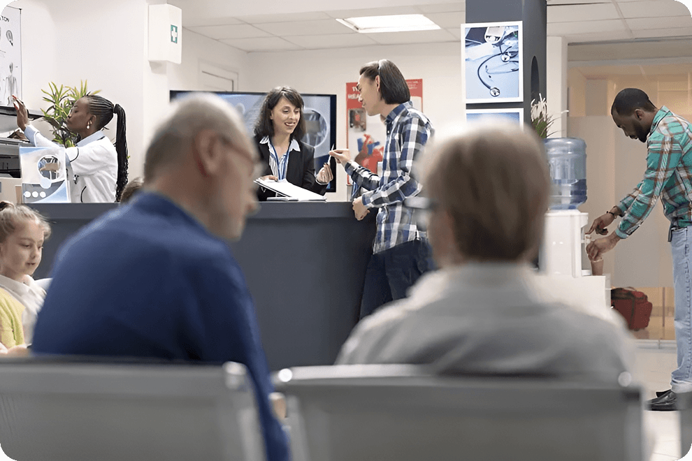 A receptionist assisting a patient at the front desk while others wait in the foreground.